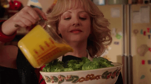 Beverly from TV Show "The Goldbergs" pouring cheesy sauce over broccoli