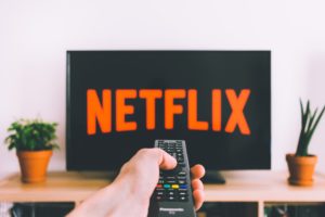 TV with Netflix displayed and person holding remote