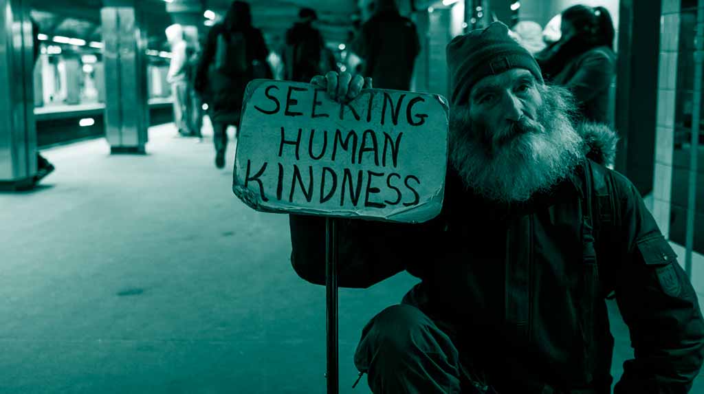 White man with gray beard holding sign in subway that reads "Seeking human kindness"