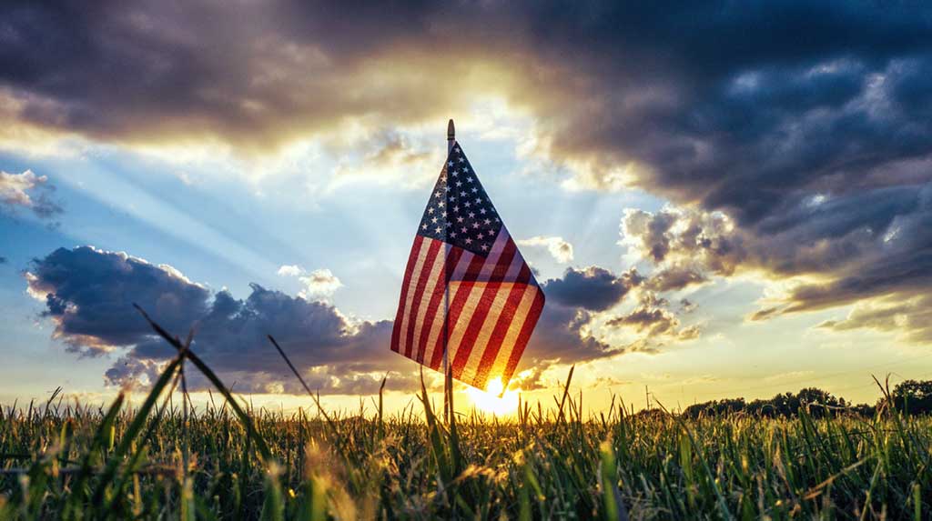 small American flag planted in the grass with sunset behind it
