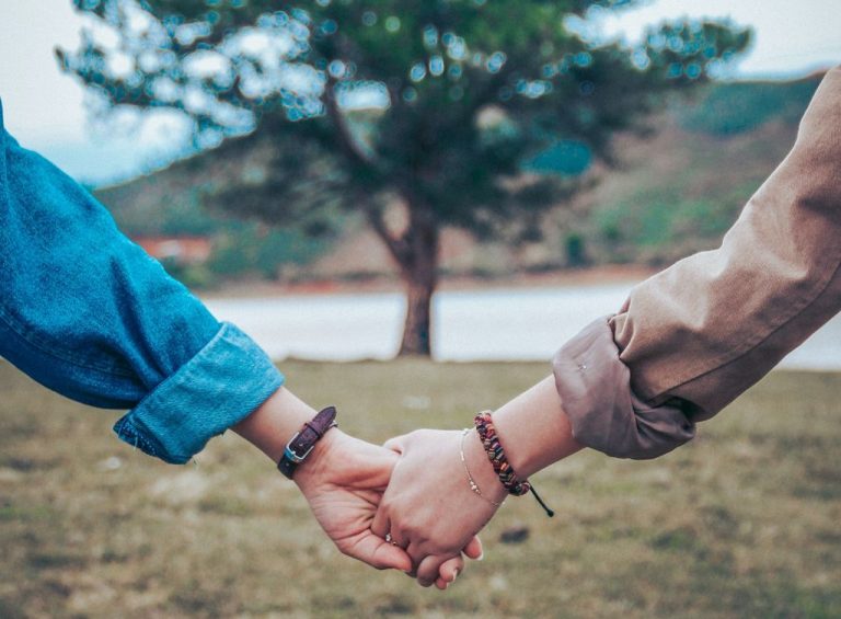 Two people hold hands in front of a tree.