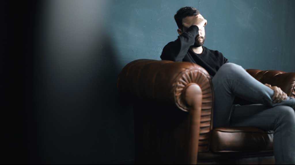 white man with hand on his face sitting on a couch