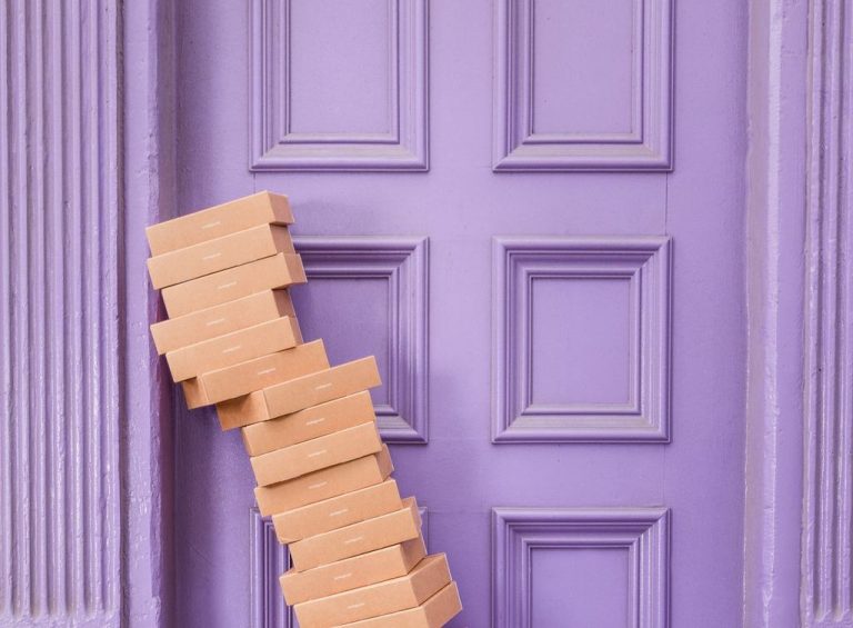 A stack of ecommerce shipping boxes sits in front of a purple door.