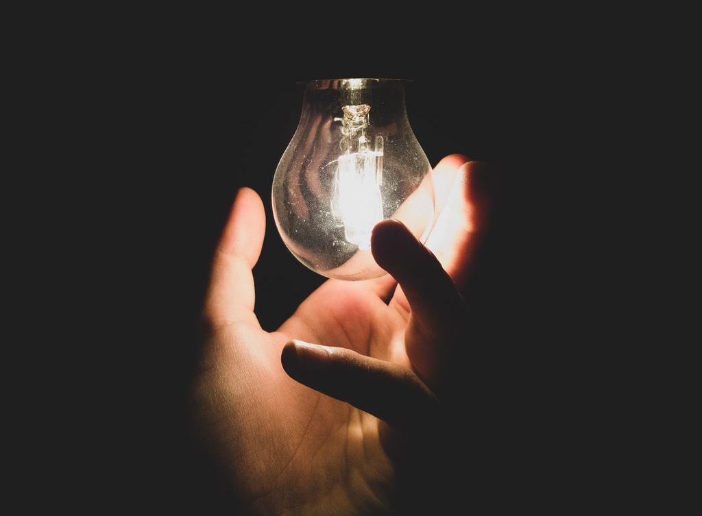 A hand holds an illuminated lightbulb.