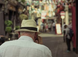 An older man in a straw hat makes a call in a narrow street.