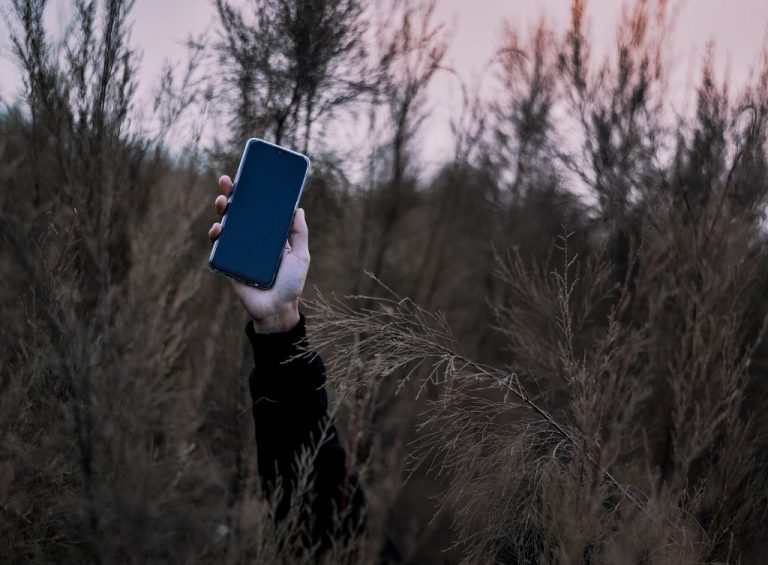 A person with their face hidden holds up a smartphone.