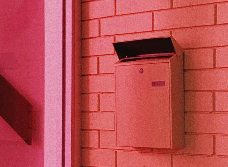 A pink mailbox on a pink wall.