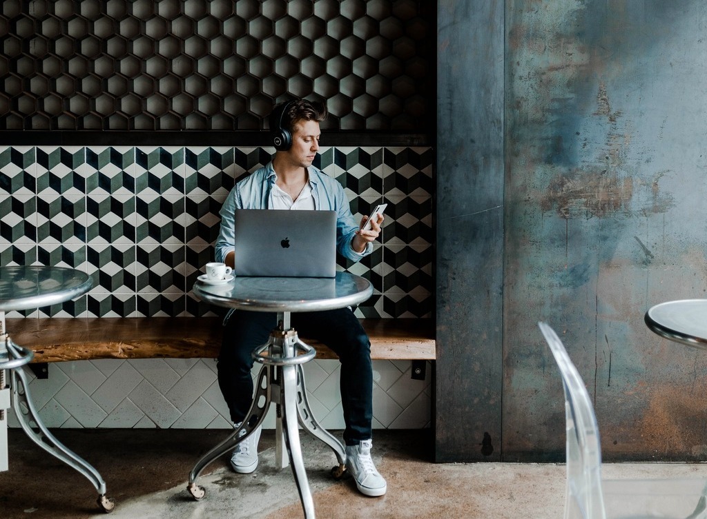 A man sitting at a laptop checks his smartphone.