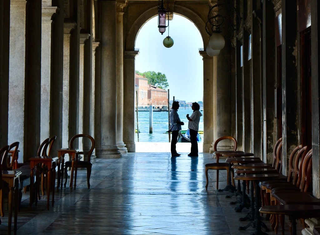 Two people are shown talking in an alleyway by the ocean.