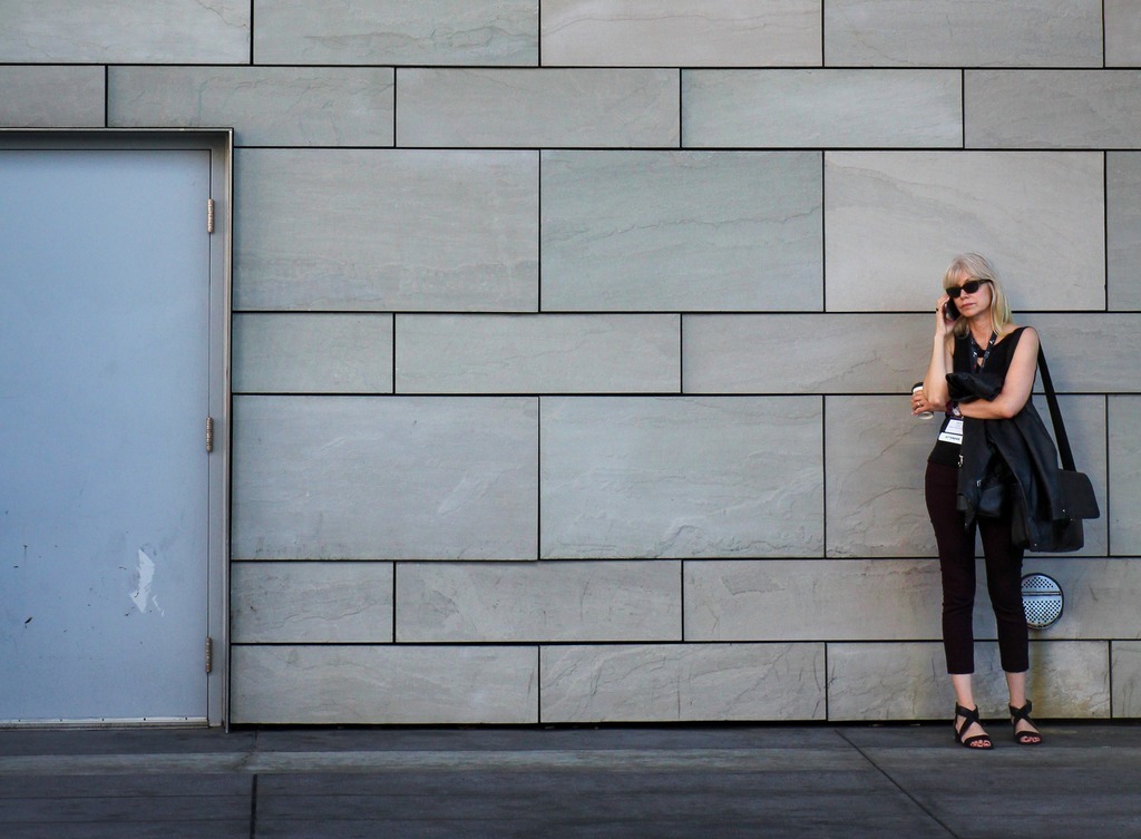 A woman stands against a wall talking on a smartphone.