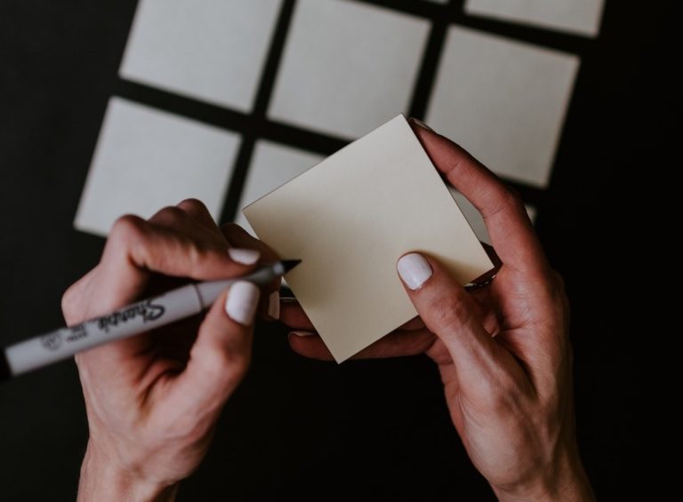 A person's hands write on a Post-It note.