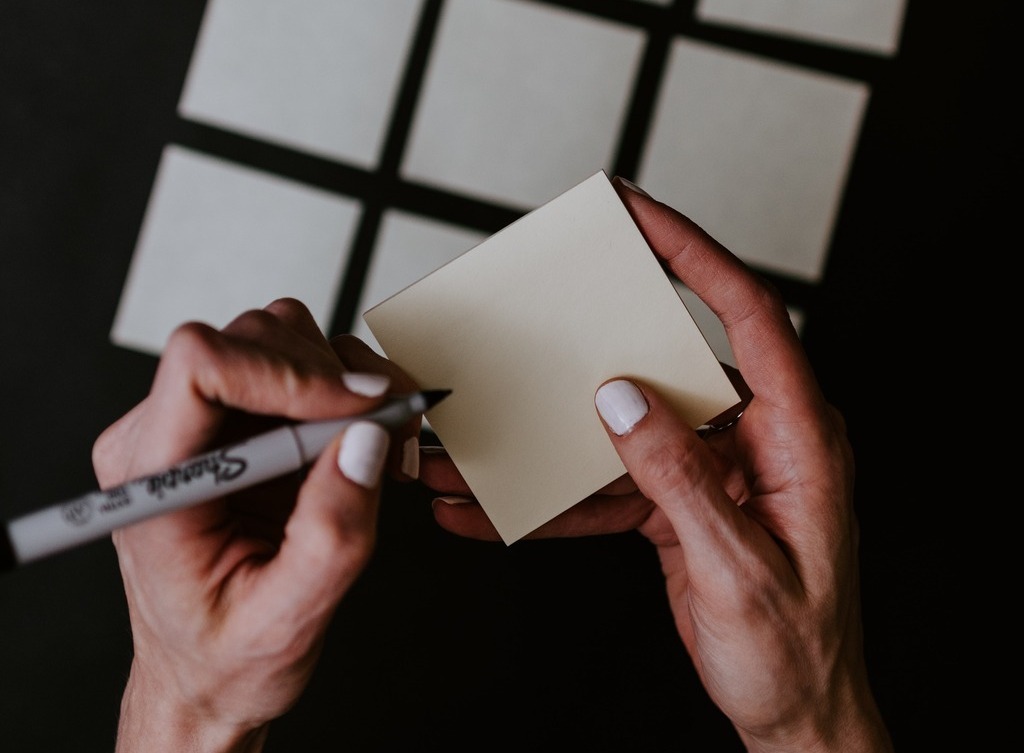 A person's hands write on a Post-It note.