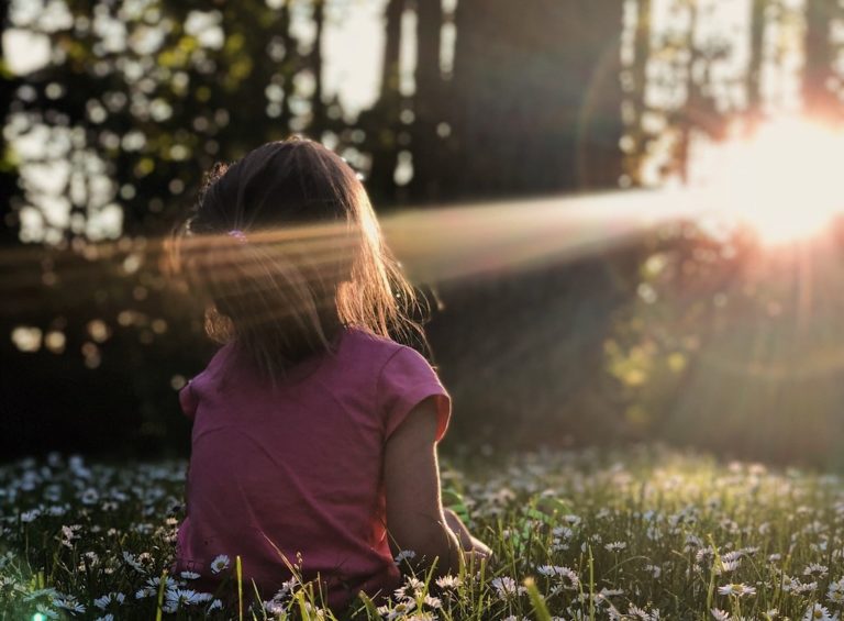 A girl sits with her back to the camera facing the sun.