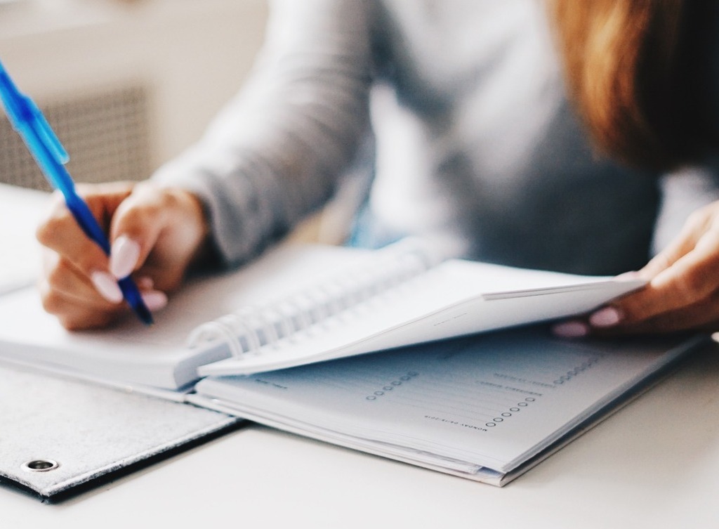 A woman's hands writing in a calendar book.