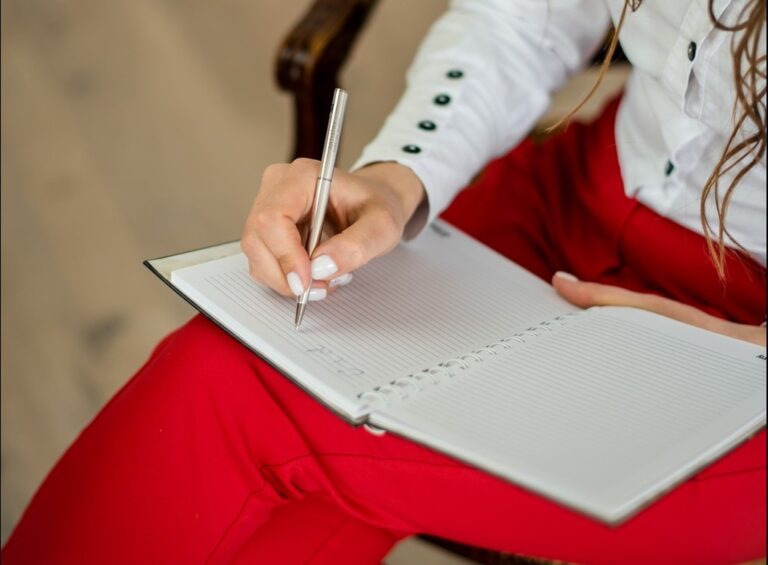 A woman holds a notebook on her lap, ready to write.